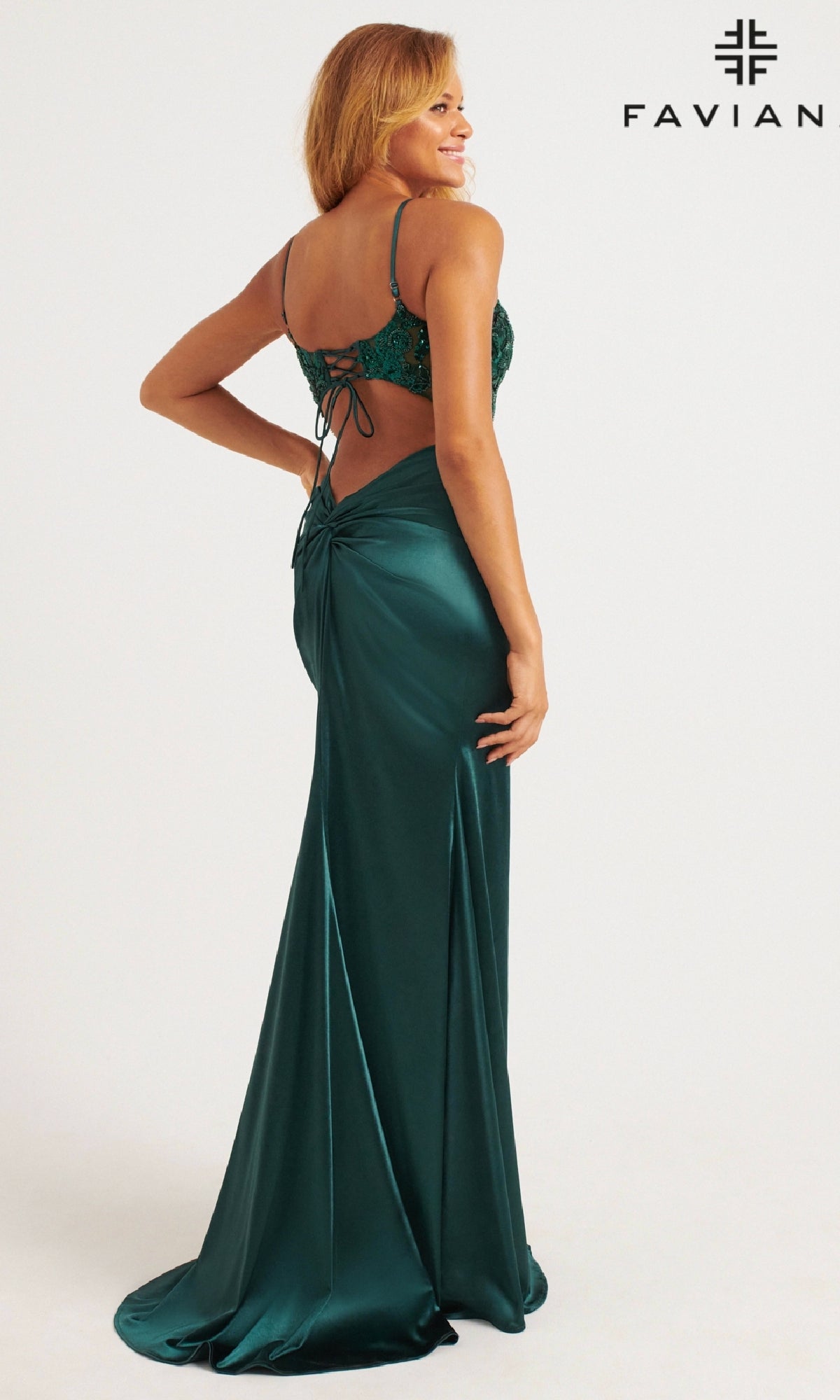 A woman confidently poses against a white background wearing the Faviana 11200 Sequin-Bodice Lace-Up Long Prom Dress in emerald green satin.